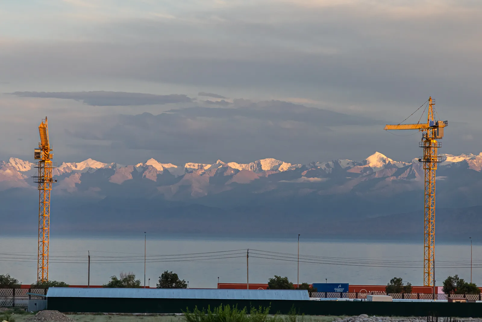 Grues à tour sur le chantier de la Tamchy SFIT face au lac Issyk-Koul et aux montagnes enneigées